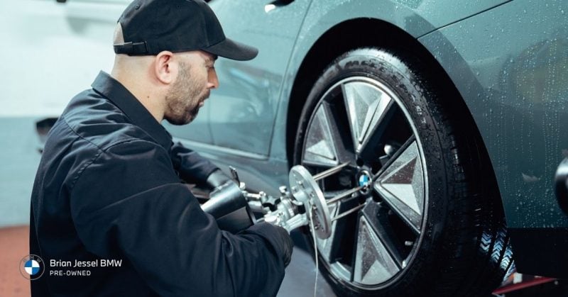 BMW technician performing wheel alignment service, highlighting professional maintenance, diagnostics, tire service, and repair support expertise.