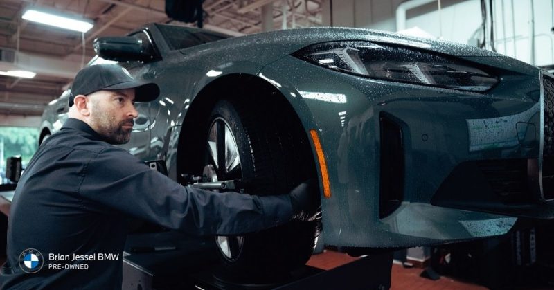 BMW technician inspecting electric vehicle suspension and tires, highlighting maintenance, repair risks, and used BMW EV ownership considerations.