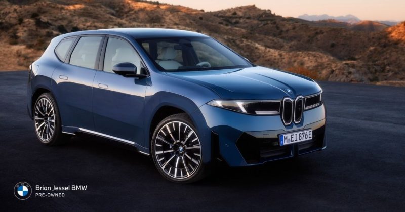 Blue BMW iX parked on a scenic mountain road at sunset