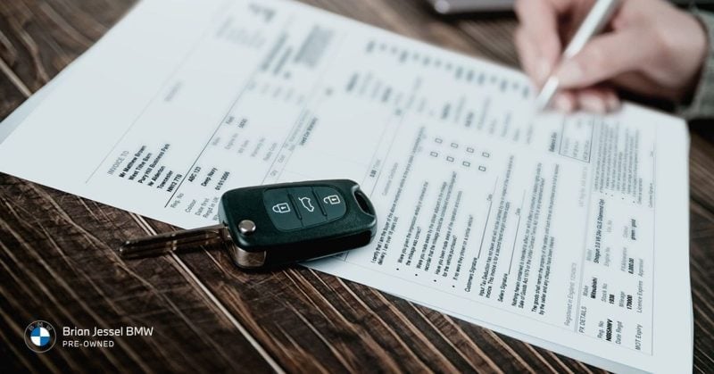 BMW warranty paperwork and key fob representing new versus pre-owned coverage options and ownership cost considerations