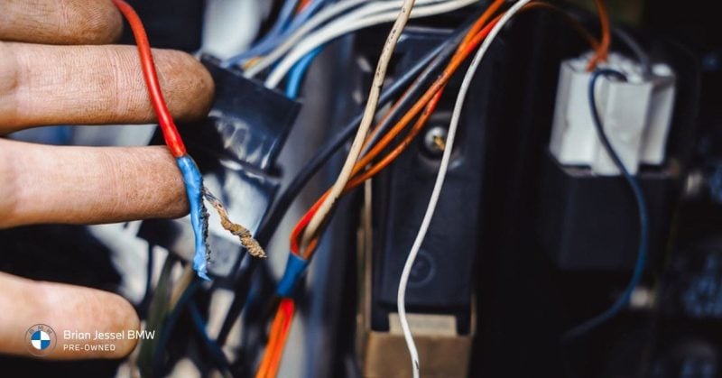 Technician inspecting damaged BMW electrical wiring, highlighting diagnostic repairs, maintenance coverage, and unexpected vehicle service issues.