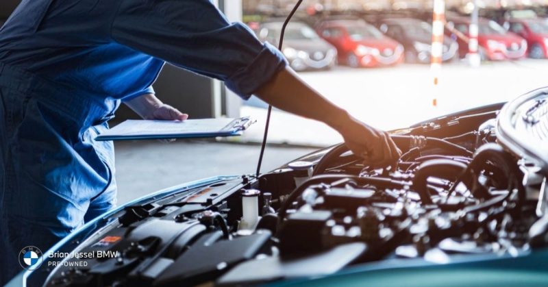 Technician inspecting BMW engine bay with checklist, emphasizing service records, professional inspections, and evaluating used vehicle condition carefully.
