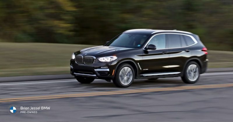 Black BMW X3 SUV driving on a road with motion blur, showcasing its sleek design and sporty presence.