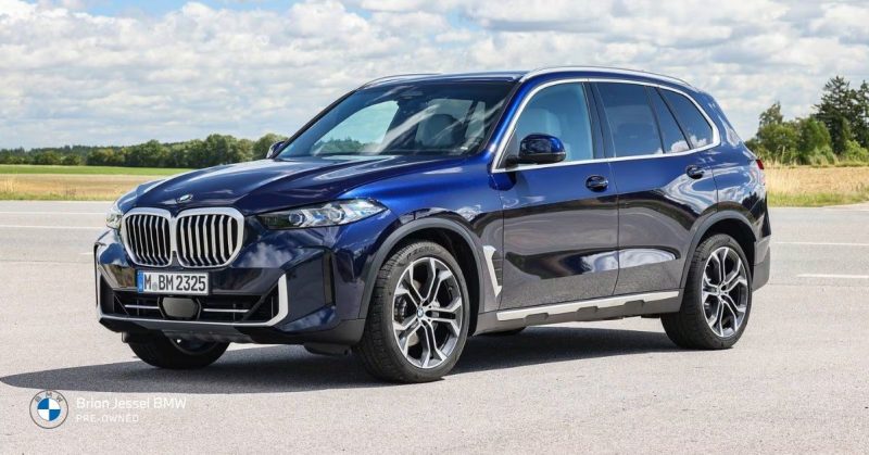 Dark blue BMW X5 SUV parked on a paved road under a bright partly cloudy sky, highlighting its sleek and commanding presence