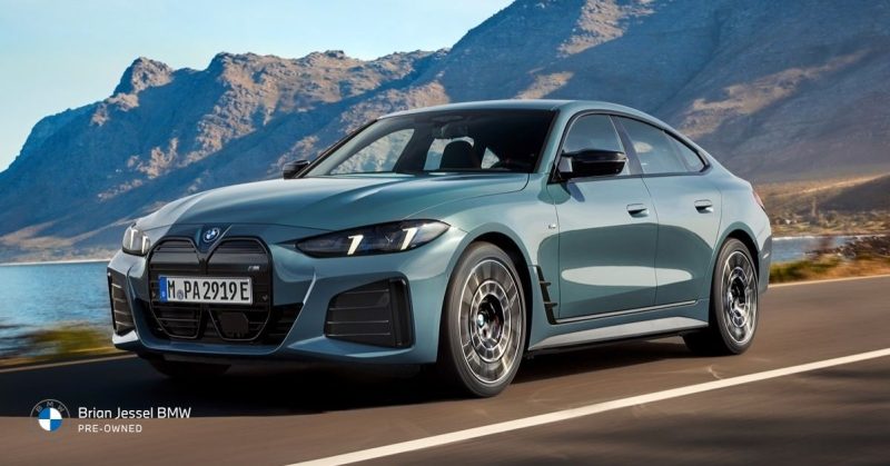 Light blue BMW 4 Series Gran Coupe driving on a scenic coastal road with mountains and water in the background