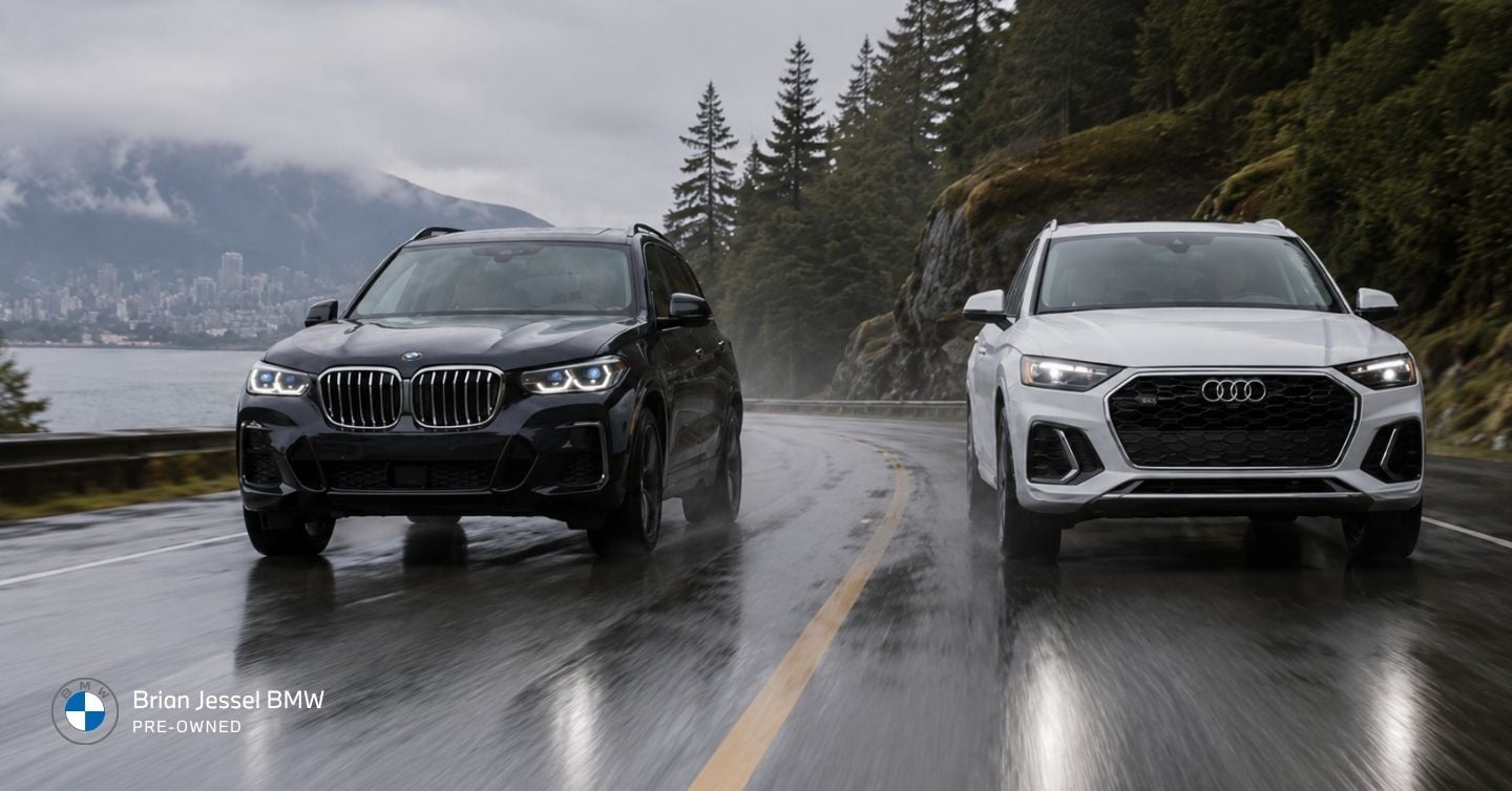 BMW X3 and Audi Q5 driving side by side on a wet Vancouver mountain road during rainy conditions.