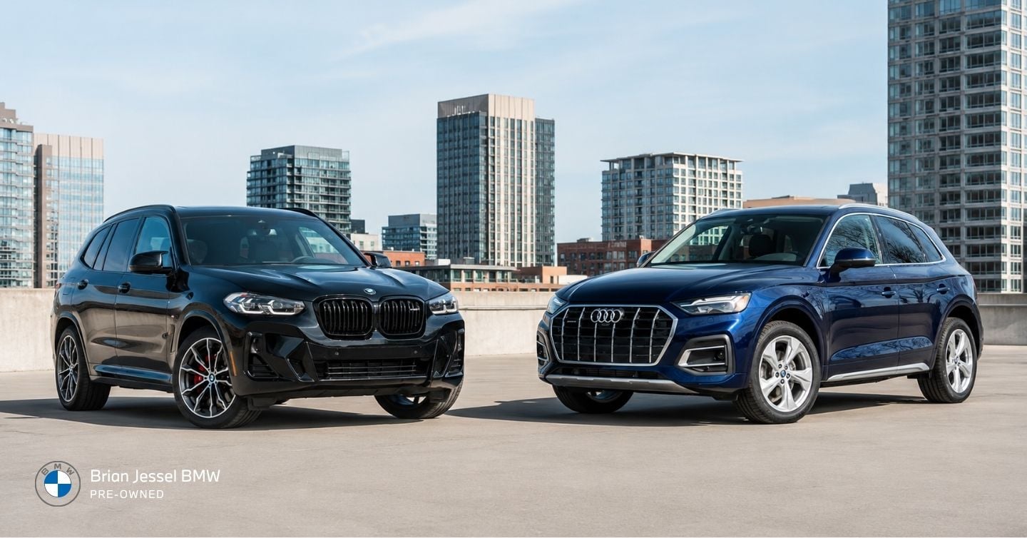BMW X3 and Audi Q5 parked side by side on an urban rooftop with city buildings.