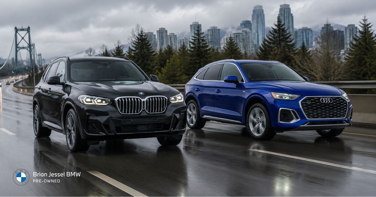 2023 BMW X3 and Audi Q5 driving through rainy Vancouver traffic with skyline backdrop on a wet urban highway
