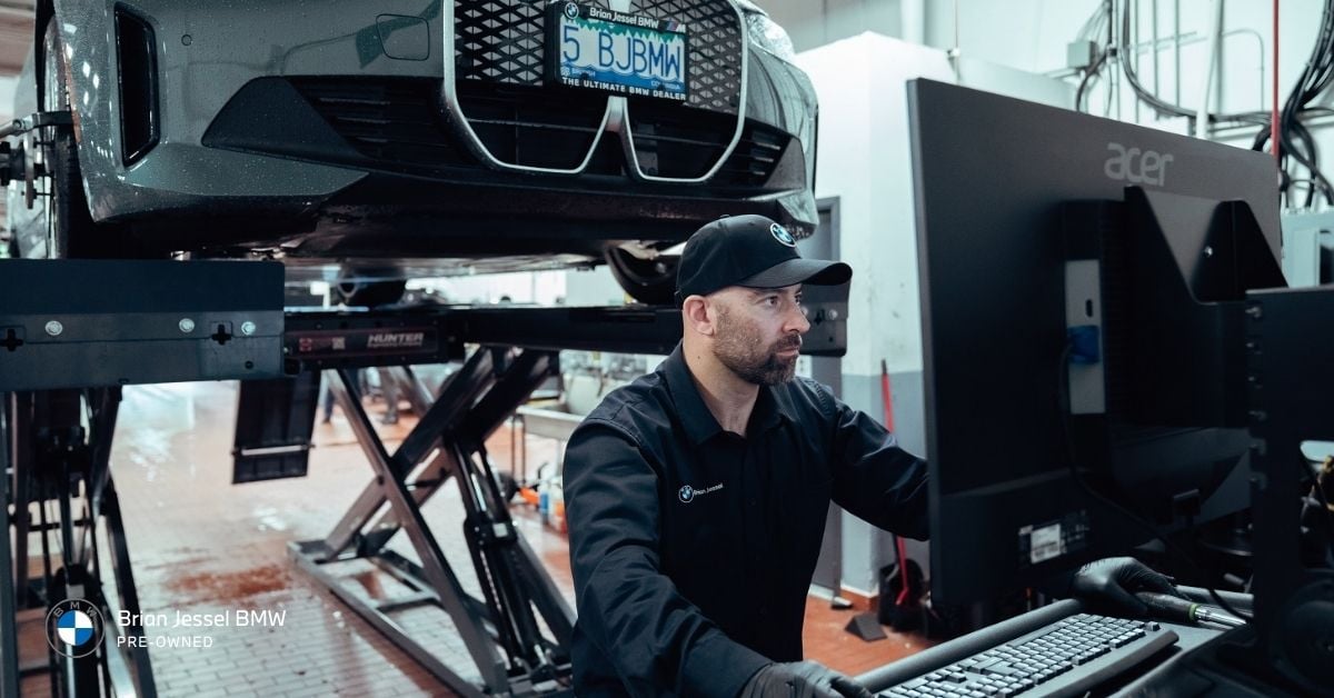 BMW Certified Service technician performing vehicle diagnostics with computer equipment inside a professional workshop.