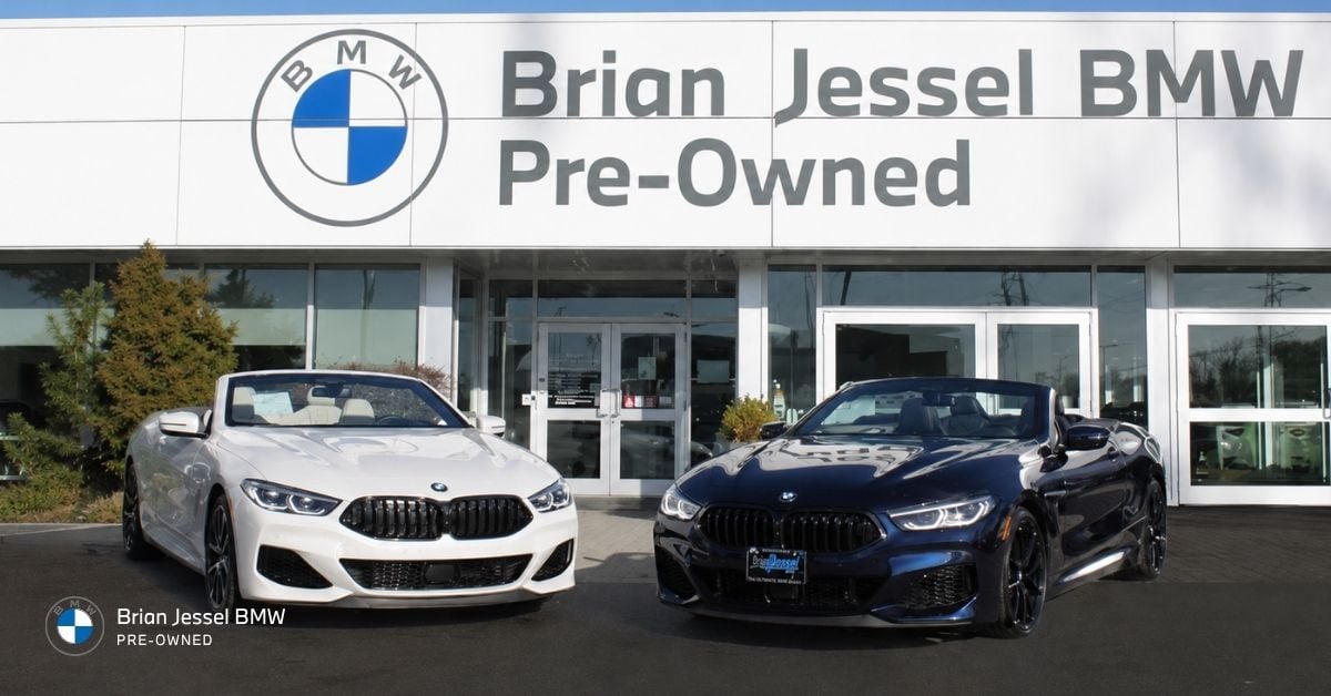 Brian Jessel BMW Pre-Owned dealership building with two luxury BMW convertibles displayed outside showroom entrance.
