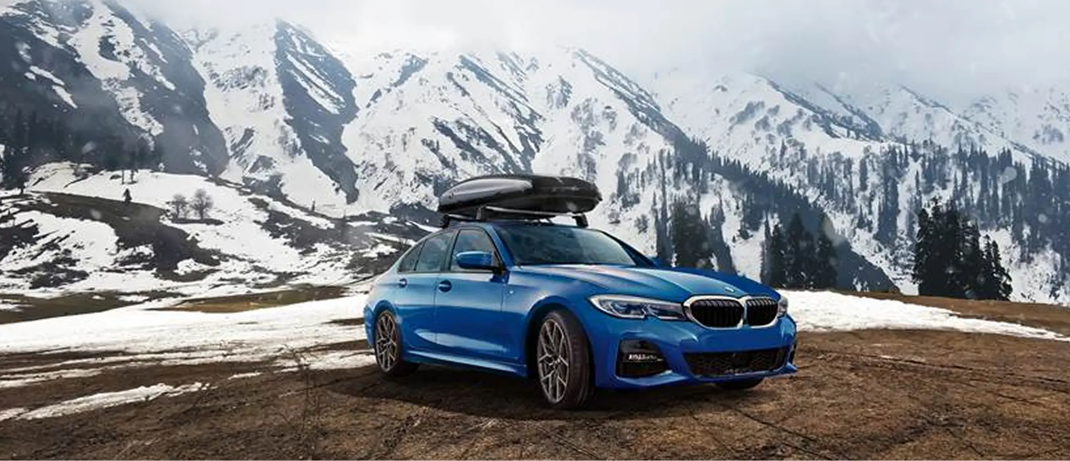 Blue BMW 330i with a roof box in the mountains